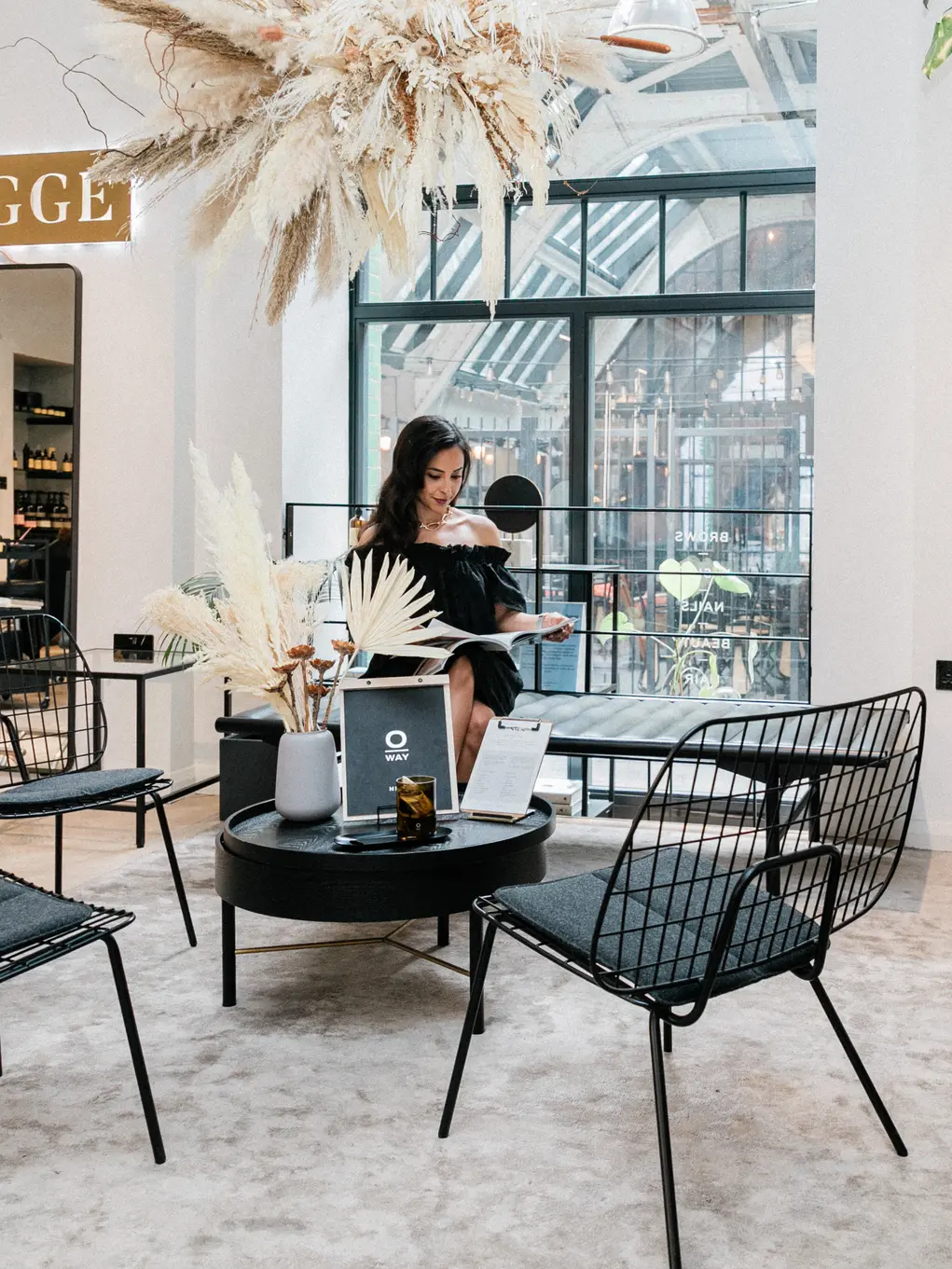 A woman sits in a beauty salon with a sign saying 'Hygge' in the background