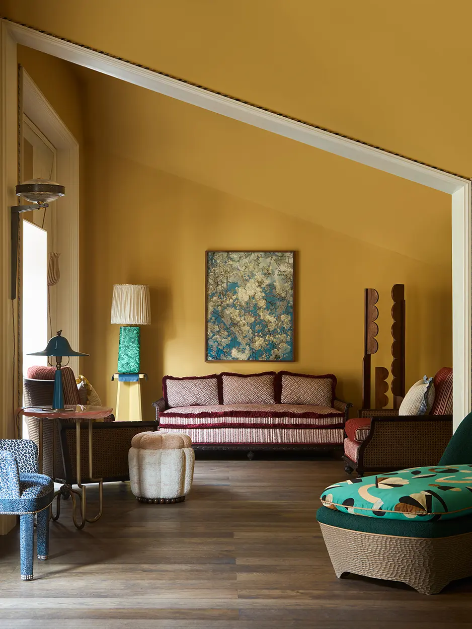 A room with yellow walls, a turquoise lamp, chaise long and pink sofa