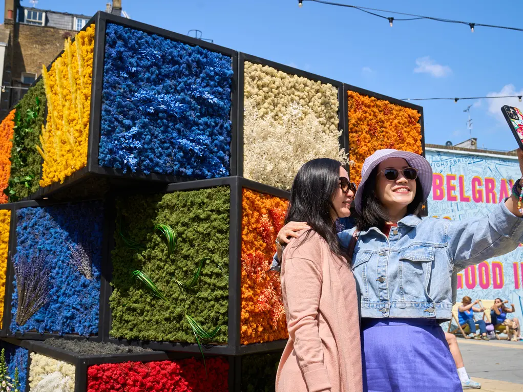 Two women take a selfie in front of a Rubik's cube flower display
