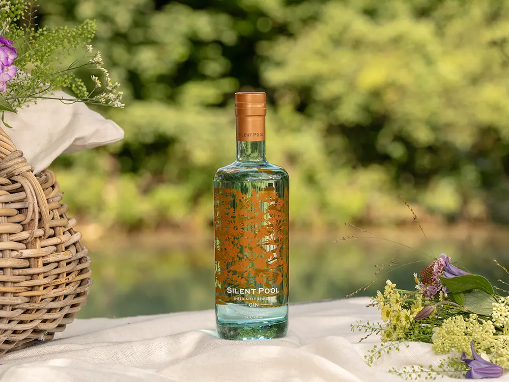 Bottle of Silent Pool gin on a table with flowers and a basket of flowers